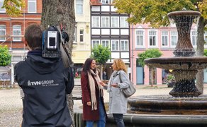 Kameramann filmt zwei Frauen, die an einem Brunnen im Stadtzentrum stehen und sich unterhalten.