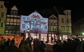 Besucher verfolgen eine großflächige Videomapping-Installation auf historischen Fassaden in der Peiner Innenstadt bei winterlicher Abendstimmung.