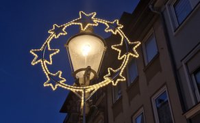 Straßenlaterne mit eingeschaltetem Licht, umgeben von einem leuchtenden Weihnachtssternkranz aus mehreren Sternen.