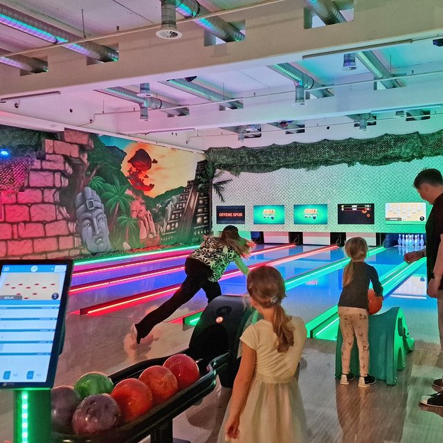 Das Bild zeigt Menschen, die auf einer Bowlingbahn spielen.