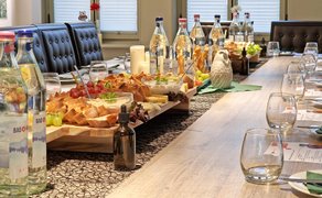 Gläser und Platten mit Brot, Käse und Obst stehen auf einem eingedeckten Tisch.