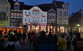 Besucher stehen auf dem Marktplatz der Peiner Innenstadt und verfolgen bei Abenddämmerung das Videomapping an den historischen Fassaden.