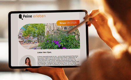 Eine Person hält ein Tablet in der Hand. Auf dem Display ist der digitale Newsletter „Peine erleben“ geöffnet, der mit Bildern und Beiträgen zu Veranstaltungen, Freizeitangeboten und Erlebnissen in Peine gefüllt ist. Im Hintergrund ist eine unscharfe grüne Parklandschaft zu sehen.