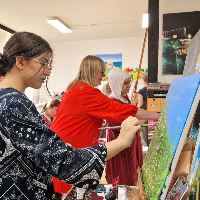 Ein Mädchen malt in einem Atelier auf einer Leinwand. 