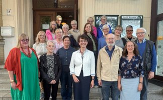 Gruppenfoto von rund 20 Personen unterschiedlichen Alters, die vor einem Gebäude gemeinsam für die Kamera posieren.