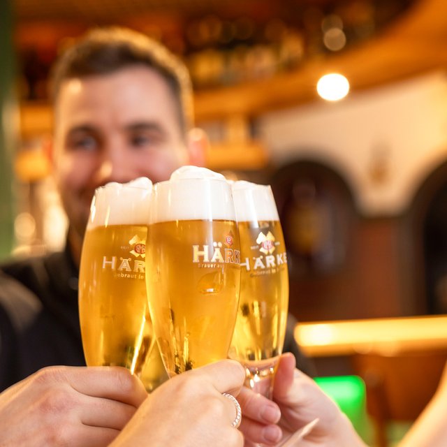 Das Bild zeigt zwei junge Menschen, die miteinander mit einem Bier anstoßen. 