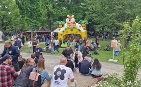 Familienfreundliches Treiben beim Highland Gathering im Park: Besucher sitzen und flanieren auf den Wegen, Kinder spielen auf einer bunten Hüpfburg mit Tiger-Motiv, umgeben von Marktständen und viel Grün – lebendiges Open-Air-Festival für alle Generationen.