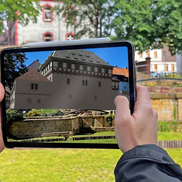 Augmented-Reality-Darstellung der Peiner Burg in der Peiner Innenstadt, angezeigt auf einem Tablet im Burgpark