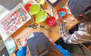 Zwei Kinder mit Baseballkappen sitzen an einem Tisch und verzieren bunte Weihnachtsplätzchen mit Zuckerguss.