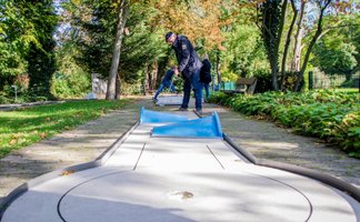 Personen spielen Minigolf auf einer Bahn im Grünen in Peine bei herbstlicher Umgebung.