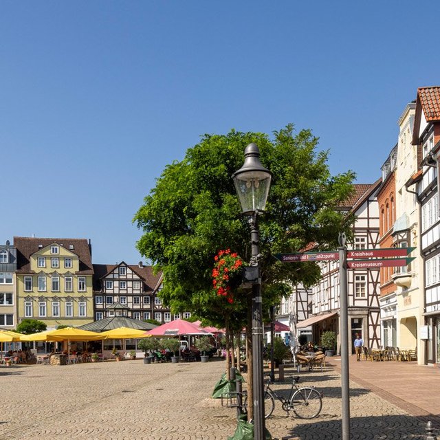 Blick über den Marktplatz in der Peiner Innenstadt mit historischen Fachwerkhäusern, Cafés, Bäumen und Kopfsteinpflaster bei sonnigem Wetter