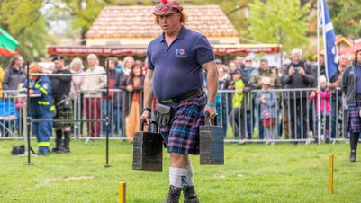 Mann in kariertem Kilt trägt schwere Gewichte beim Highland-Gathering vor Zuschauern im Peiner Stadtpark