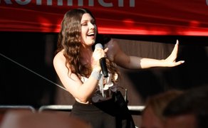 Eine Sängerin hält ein Mikrofon in der Hand und singt auf einer Bühne.