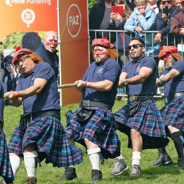 Gruppe von Männern in Kilts und karierten Mützen mit Bommel zieht gemeinsam an einem Tau im Peiner Stadtpark.