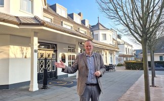 Mann in Sakko steht vor einem mehrstöckigen Hotelgebäude mit Innenhof.