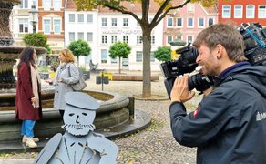 Kameramann filmt zwei Frauen, die an einem Brunnen im Stadtzentrum stehen und sich unterhalten.