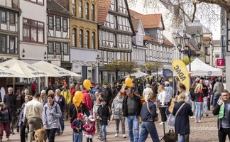 Viele Menschen besuchen eine belebte Fußgängerzone mit Fachwerkhäusern, Aktionsständen und orangefarbenen Luftballons in der Innenstadt von Peine.
