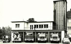 Historische Schwarz-Weiß-Aufnahme der alten Feuerwache in der Burgstraße in Peine. Vor dem Gebäude mit seinem hohen Schlauchturm stehen mehrere historische Feuerwehrfahrzeuge.