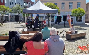 Das Bild zeigt das Publikum, das vor der OpenStage auf der Stadtoase auf dem Historischen Marktplatz in Peine Platz genommen hat. 