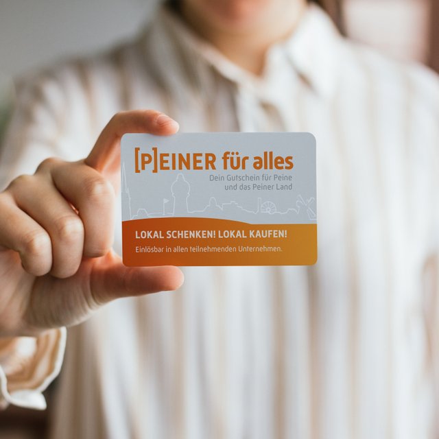 Eine Person hält den Gutschein „[P]EINER für alles“ in die Kamera – ein lokaler Geschenkgutschein für Peine und das Peiner Land.