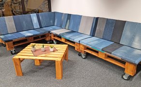 Ecksofa aus Holzpaletten auf Rollen mit aus Jeans gefertigten Polstern, davor ein kleiner Holztisch.