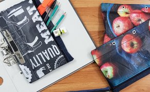 Aus bunt bedruckter Folie und Stoff gefertigte Federmappen mit Lochung zum Einheften auf einem Tisch.