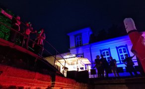 Nächtliche Silent Disco in Peine: Menschen mit leuchtenden Funkkopfhörern tanzen und stehen auf einer Brücke und vor einem farbig illuminierten Gebäude, während eine Kopfhörerparty im Freien für besondere Atmosphäre sorgt.