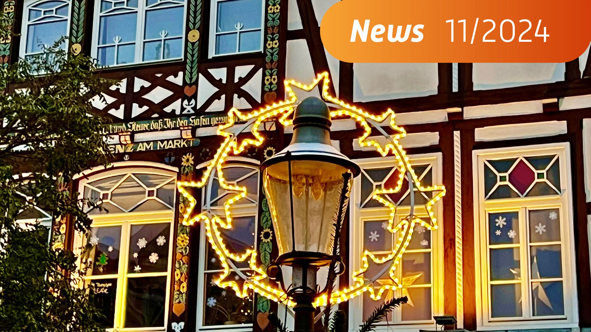 DAs Bild zeigt eine Weihnachtsbeleuchtung in Nahaufnahme, im Hintergrund befindet sich ein weihnachtlich geschmücktes Fachwerkhaus. 