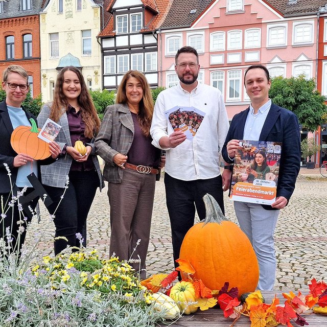 Gruppenfoto auf dem Historischen Marktplatz in Peine: Fünf Personen stehen hinter einer herbstlich dekorierten Bank mit Kürbis, Blumen und buntem Laub