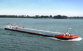 Das Bild zeigt ein fahrendes Binnenschiff mit Solarzellen auf der Abdeckung des Frachtraums.
