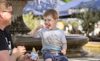 Das Bild zeigt einen Jungen, der ein Eis isst und am Brunnen am Historischen Marktplatz in Peine sitzt.