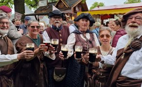 Gruppe fröhlicher Besucher in historisch-schottischer Kleidung stößt beim Highland Gathering mit Guinness-Bier an und feiert gemeinsam auf dem Festivalgelände.