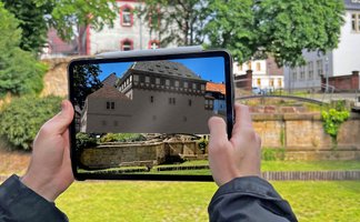 Augmented-Reality-Darstellung der Peiner Burg in der Peiner Innenstadt, angezeigt auf einem Tablet im Burgpark