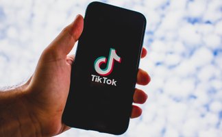 Das Bild zeigt eine Hand, die ein Handy hält, und auf dem das Logo der Plattform Tiktok zu sehen ist. 