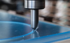 Nahaufnahme eines Fräsers, der eine blaue Kunststoffplatte bearbeitet.