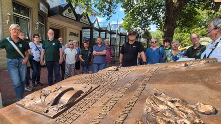 Eine Gruppe steht vor einem Gebäude und betrachtet eine große bronzene Buchskulptur.
