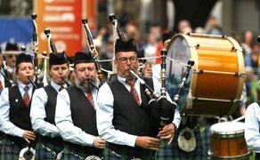Dudelsackkapelle beim Highland Gathering: Musiker in traditioneller schottischer Tracht mit Kilts spielen im Gleichschritt Dudelsäcke, begleitet von einer großen Trommel – eindrucksvolle Parade vor Publikum.