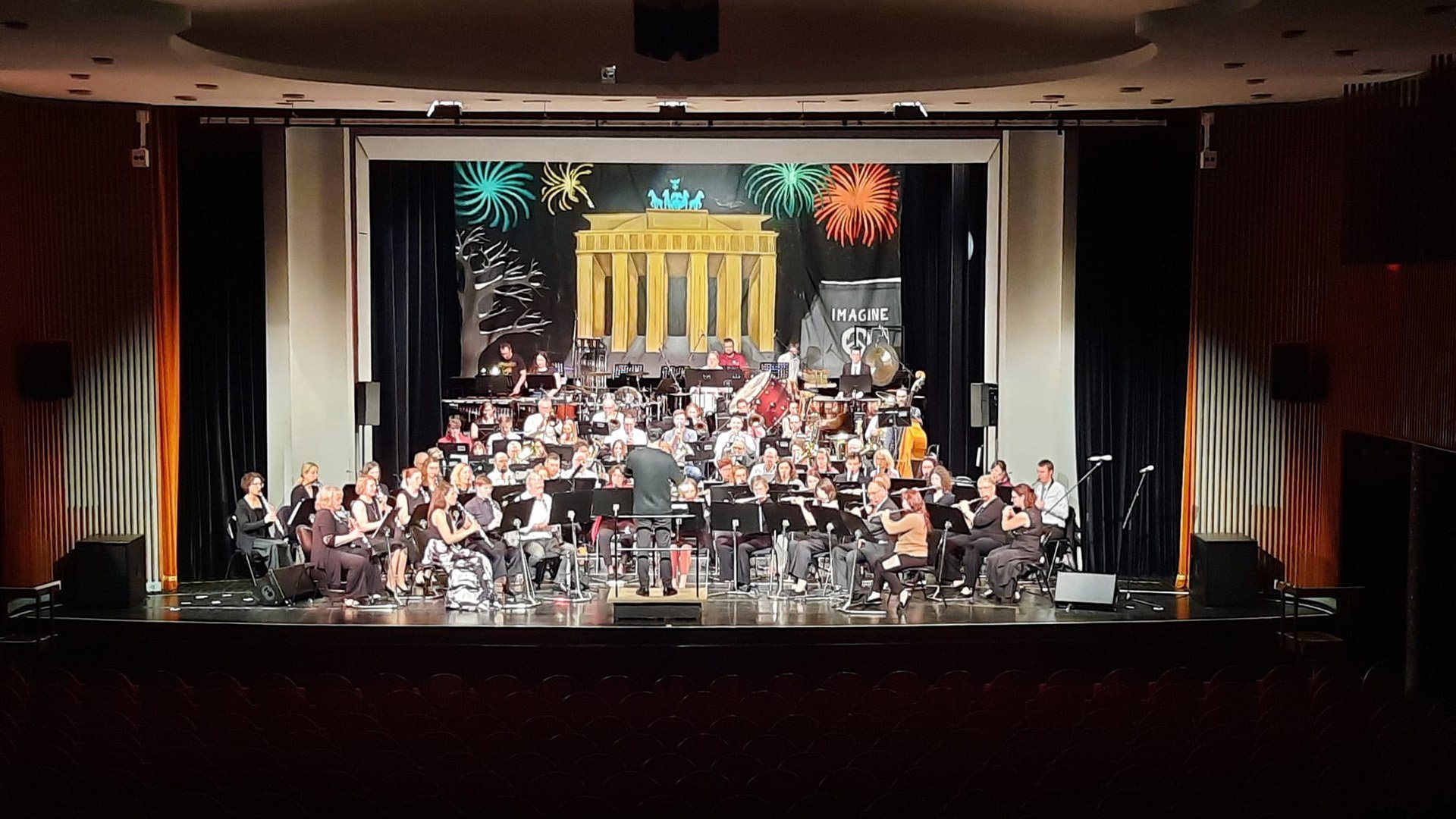 Orchester auf Bühne mit Dirigent, im Hintergrund Bühnenbild mit Brandenburger Tor und Feuerwerk.