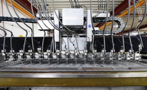 Industrielle Maschine mit mehreren Düsen und Kabeln in einer Fertigungshalle.