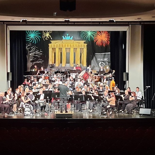 Orchester auf Bühne mit Dirigent, im Hintergrund Bühnenbild mit Brandenburger Tor und Feuerwerk.