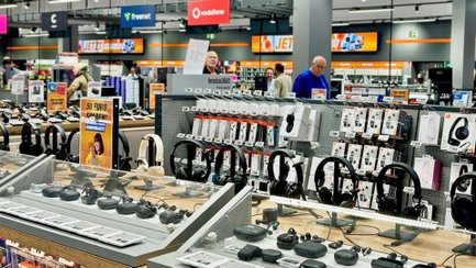 Innenansicht eines Elektronikmarkts mit Verkaufsflächen für Smartphones, Kopfhörer und weiteres Elektronikzubehör.
