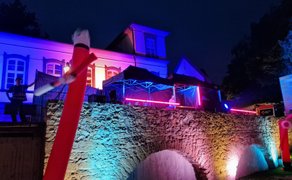 DJ-Stage bei einer Silent Disco in Peine auf einer historischen Steinbrücke, mit farbig beleuchtetem Gebäude, Neonlichtern und roten aufblasbaren Tanzfiguren bei Nacht.