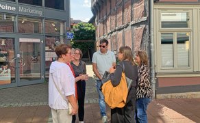 Eine Gruppe von Menschen steht vor einem Fachwerkhaus und einem Anbau mit der Aufschrift Tourist-Information.
