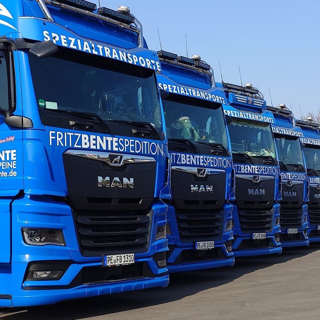 Reihe blauer Sattelzugmaschinen der Marke MAN mit Aufschrift „FRITZ BENTE SPEDITION“ und „SPEZIALTRANSPORTE“ auf der Front, geparkt auf einem Hof.
