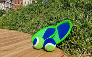 Zwei grün-blaue Wurfspiele mit passenden Bällen liegen auf einer Holzplattform vor einer bepflanzten Grünfläche; im Hintergrund sind Fachwerkhäuser und Gebäude der Peiner Innenstadt zu erkennen.