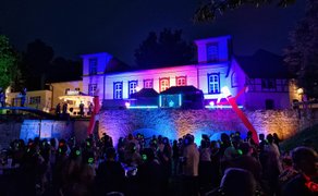 Menschen mit leuchtenden Funkkopfhörern feiern nachts vor einer bunt illuminierten historischen Kulisse im Peiner Burgpark.