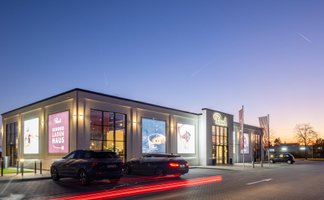 Das Rausch Schokoladenhaus Peine zeigt sich in der Abenddämmerung als modern beleuchtete Chocolaterie in Peine, mit großformatigen Schokoladenmotiven an der Fassade. Die Außenaufnahme unterstreicht Genuss, Café und Schokolade in Peine als hochwertiges Ziel für Kulinarik und Süßwaren.