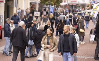 Belebte Fußgängerzone in der Peiner Innenstadt mit zahlreichen Passanten unterschiedlichen Alters, die zwischen Geschäften flanieren und einkaufen. Im Vordergrund gehen zwei junge Erwachsene durch das geschäftige Treiben der Einkaufsstraße.