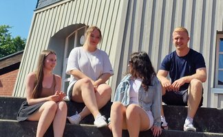 Das Bild zeigt eine Gruppe junger Menschen, die auf den Stufen vor der Töpfers Mühle in Peine sitzen. 