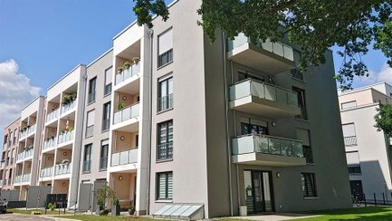 Mehrstöckiges Wohngebäude mit Balkonen und großen Fenstern, umgeben von Bäumen.